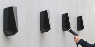 Mehrere Wallboxen an einer Wand. Man sieht eine Hand die im Begriff ist einen Stecker einzustecken.